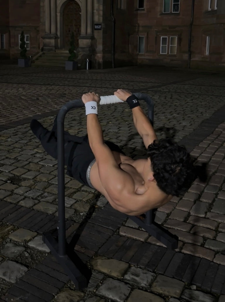 Athlete holding a front lever on parallettes at night wearing Calix black and white wristbands
