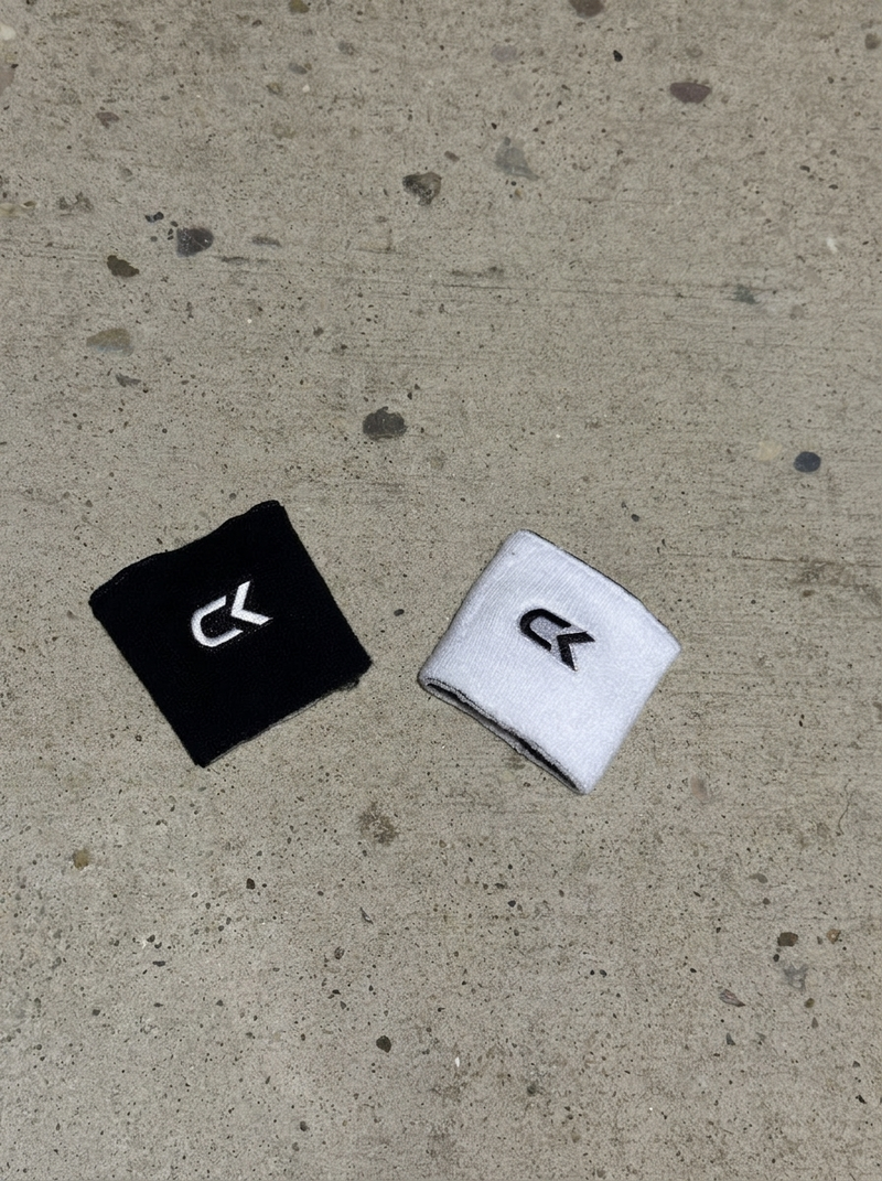Two Calix reversible wristbands on concrete, one turned black side up and one white side up, each with an embroidered CK logo