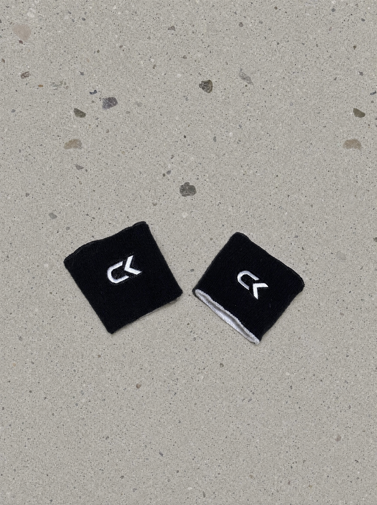Pair of Calix wristbands worn black side out with white embroidered CK logos, white terry cotton showing at the trim