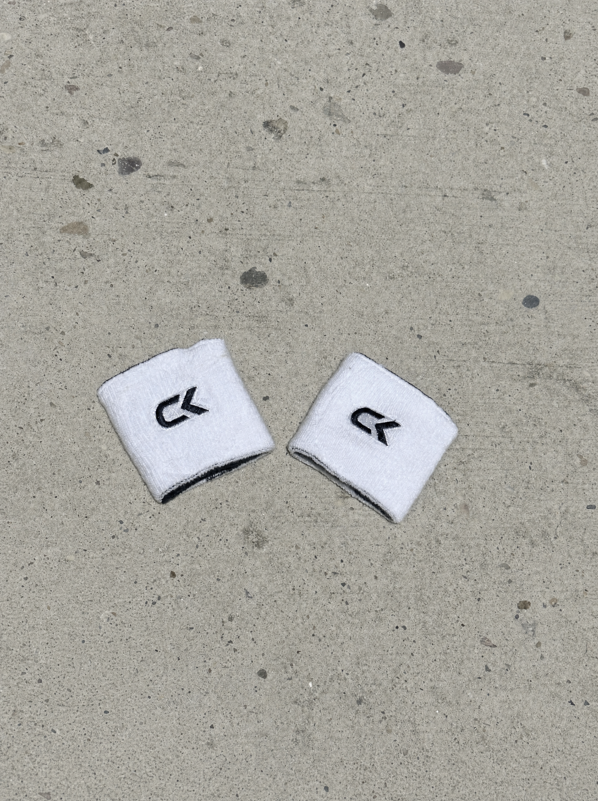 Pair of Calix wristbands turned white side out with black embroidered CK logos, laid on concrete