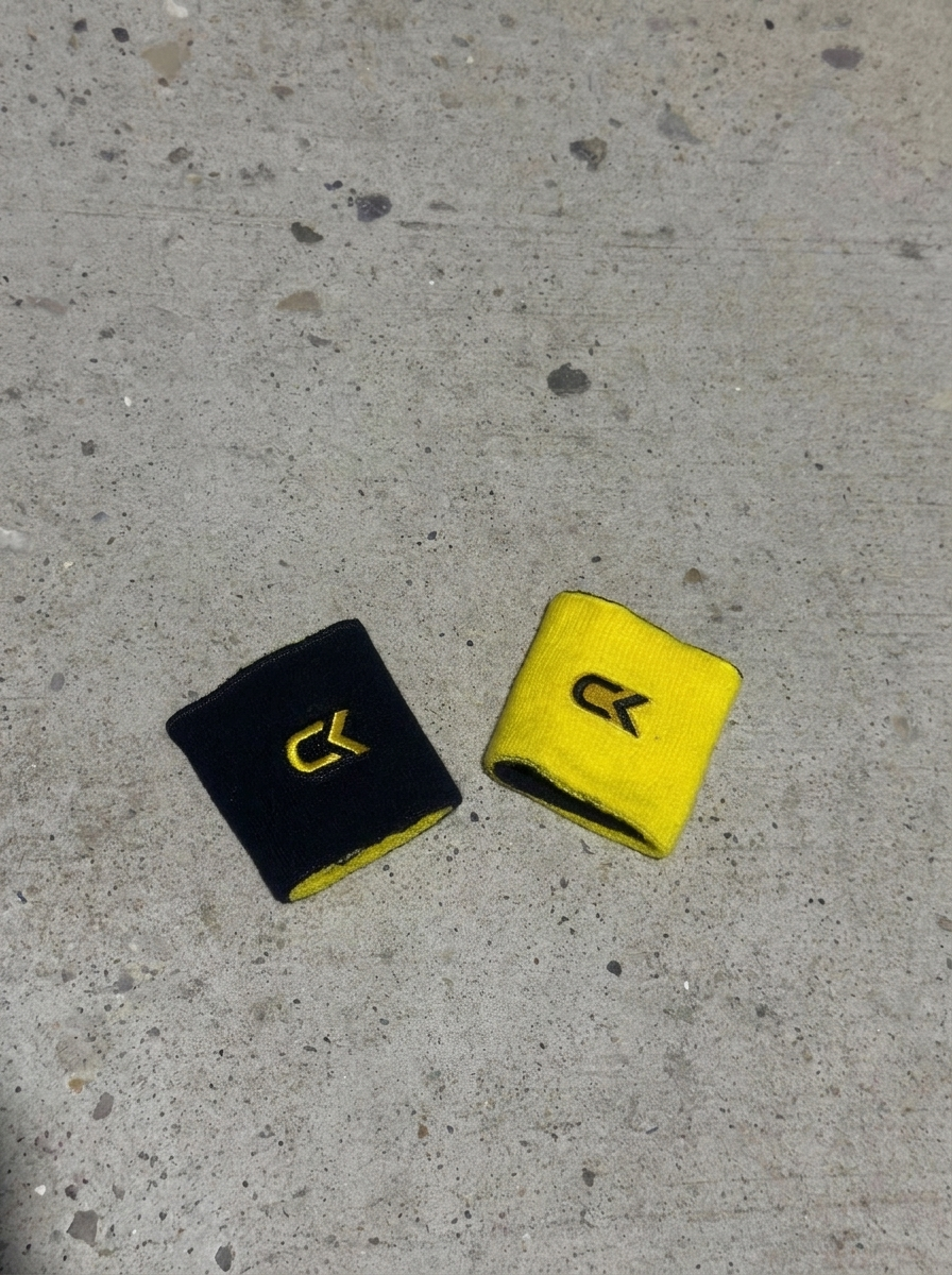 Two Calix reversible wristbands on concrete, one turned black side up and one yellow side up, each with an embroidered CK logo