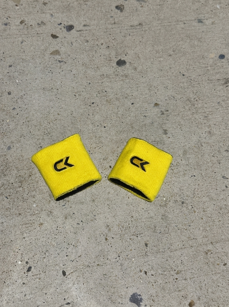Pair of Calix wristbands turned yellow side out with black embroidered CK logos, laid on concrete